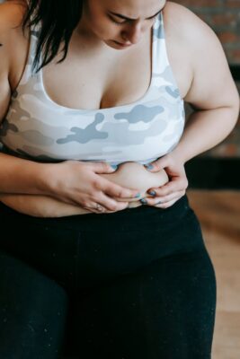 focused young overweight woman touching stomach in gym