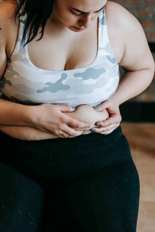 focused young overweight woman touching stomach in gym